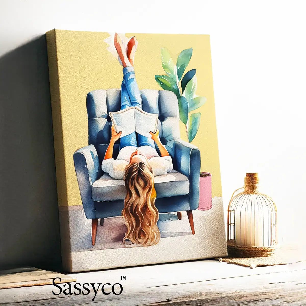 Painting of a woman reading a book in a blue armchair with 'Sassyco' branding. A yellow, blue boho style watercolor modern artwork of a woman reading book. Boho watercolor wall art painting canvas, framed art print for bedroom, living room, sitting room decor. Boho wall decor ideas for modern Indian homes. Buy wall art painting online 